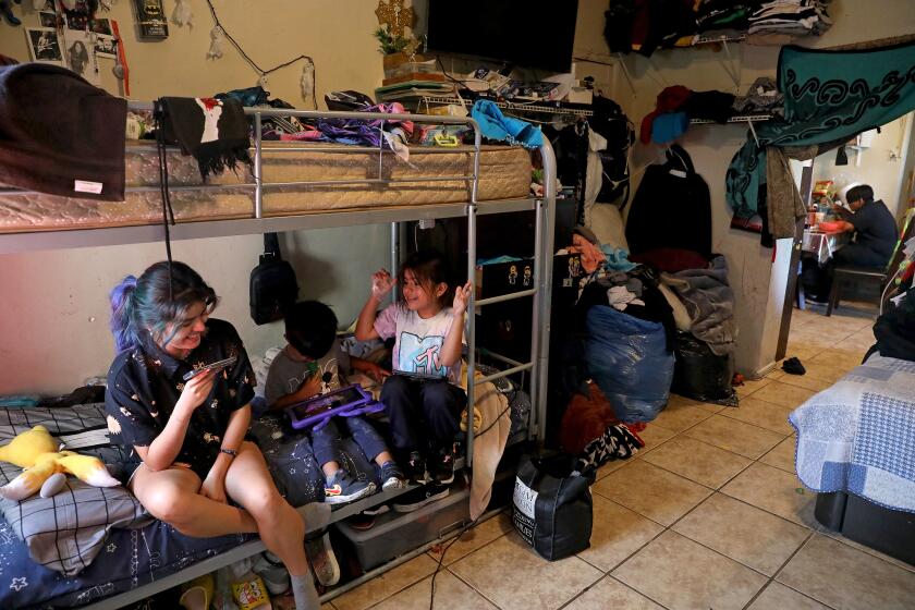 LOS ANGELES, CA - JUNE 15: Angie Davila, 20, left, the oldest of six children, plays video games with youngest siblings Lino Galicia, 3, and Yaretzi (cq) Galicia, 7, on the bunk beds in the family's one-bedroom apartment in the Pico-Union neighborhood on Wednesday, June 15, 2022 in Los Angeles, CA. There are eight family members sharing a one bedroom unit. Magdalena Garcia, 40, and husband Edgar Galicia, 48, live with their six children in a one-bedroom apartment. Magdalena has lived in the unit over 20 years. Overcrowded housing in Pico-Union, considered the most overcrowded neighborhood in Los Angeles. (Gary Coronado / Los Angeles Times)