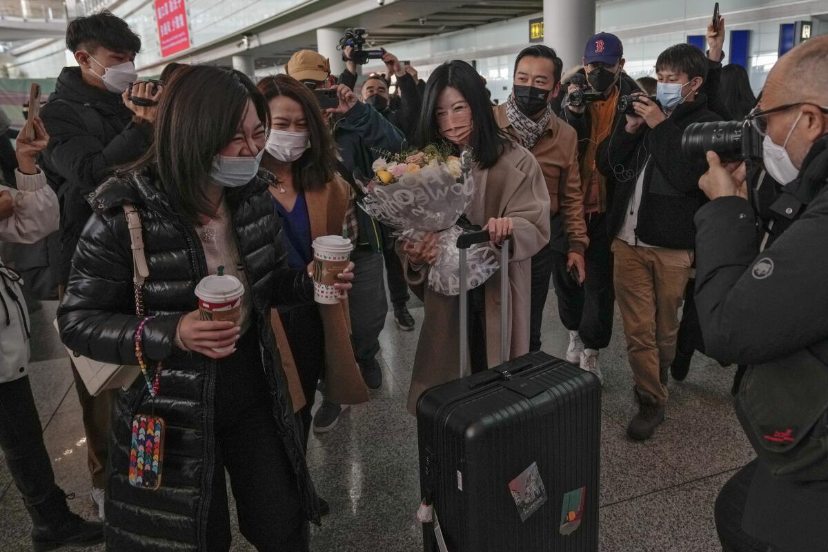 A woman holding a bouquet of flowers reacts with her relatives surrounded by journalists as she arrives from Hong Kong.