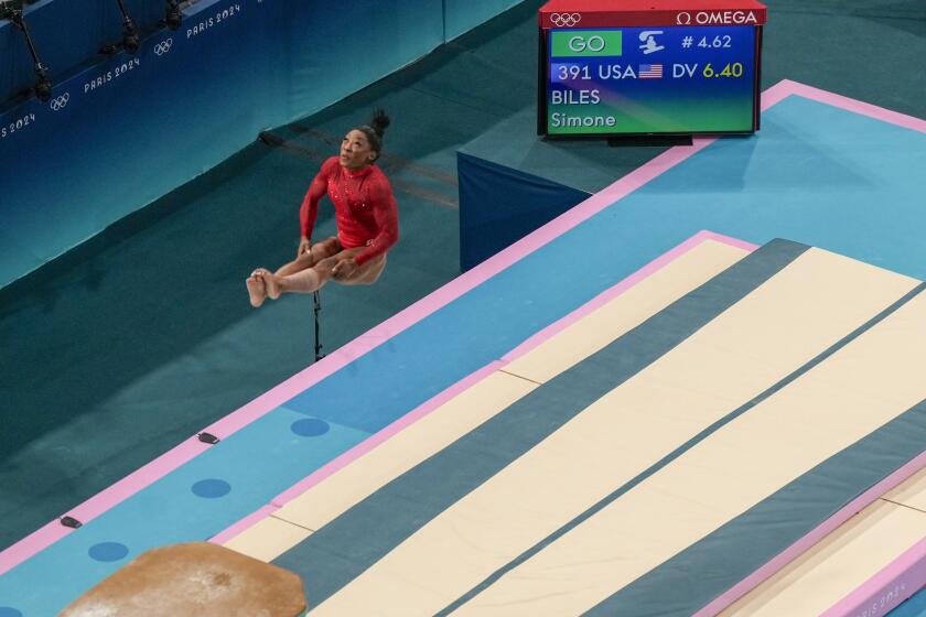 Simone Biles holds a pike position in midair, next to a monitor that displays the maneuver's 6.4 difficulty rating