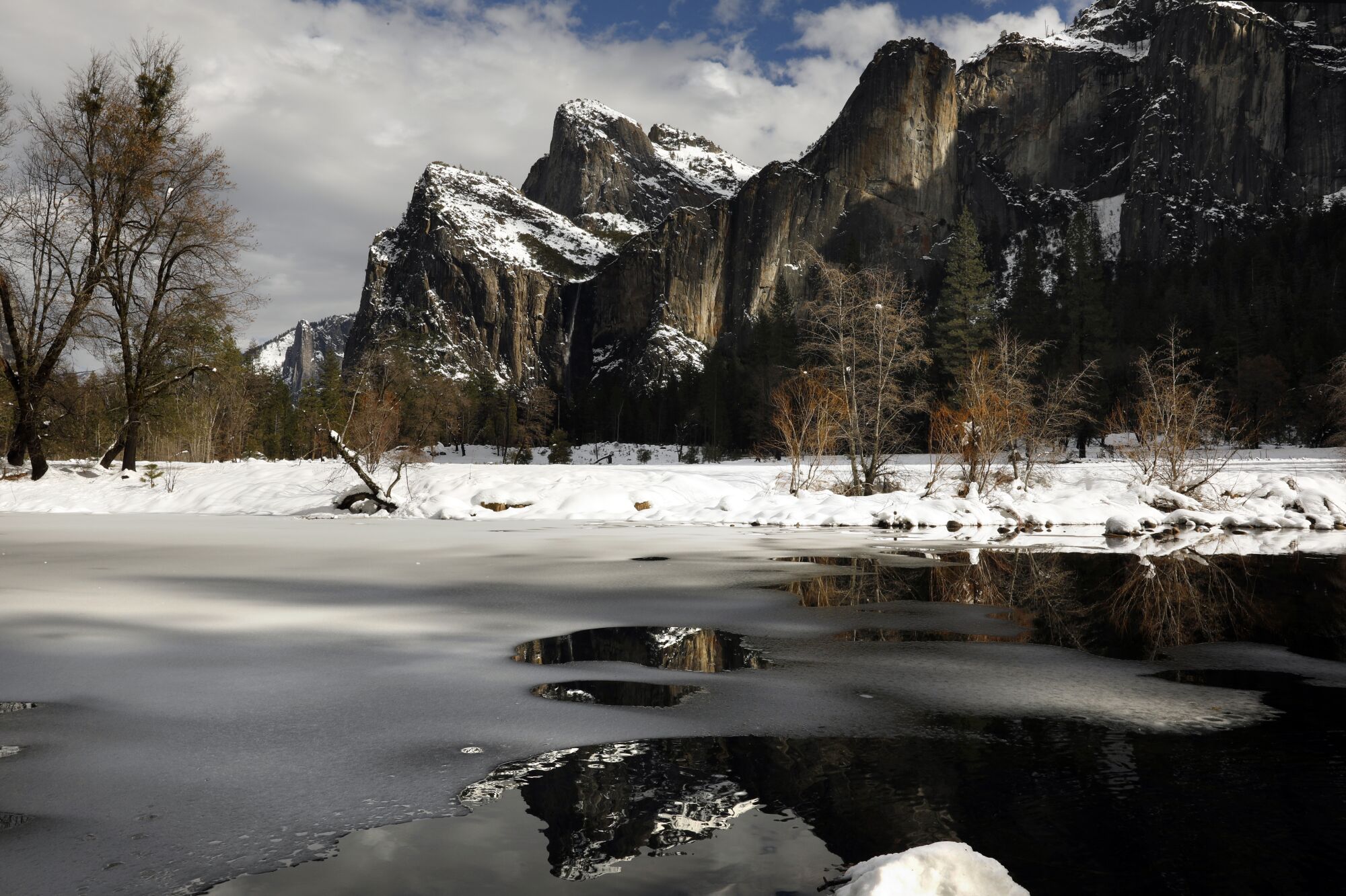 Snow-dusted Cathedral Rocks behind the partially frozen over Merced River in the Yosemite Valley.