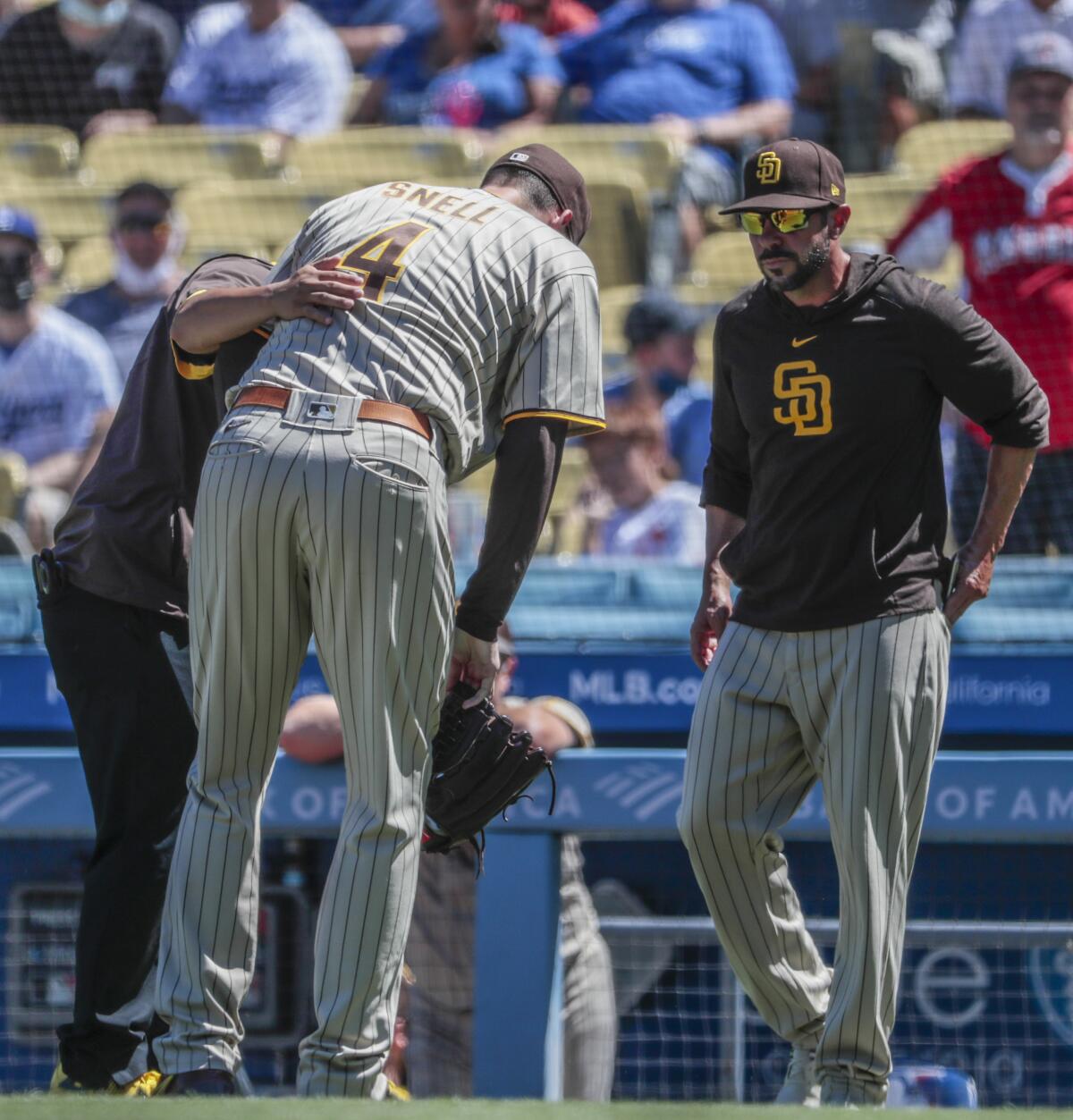 Padres starting pitcher Blake Snell (4) bends over in apparent pain as manager Jayce Tingler approaches.