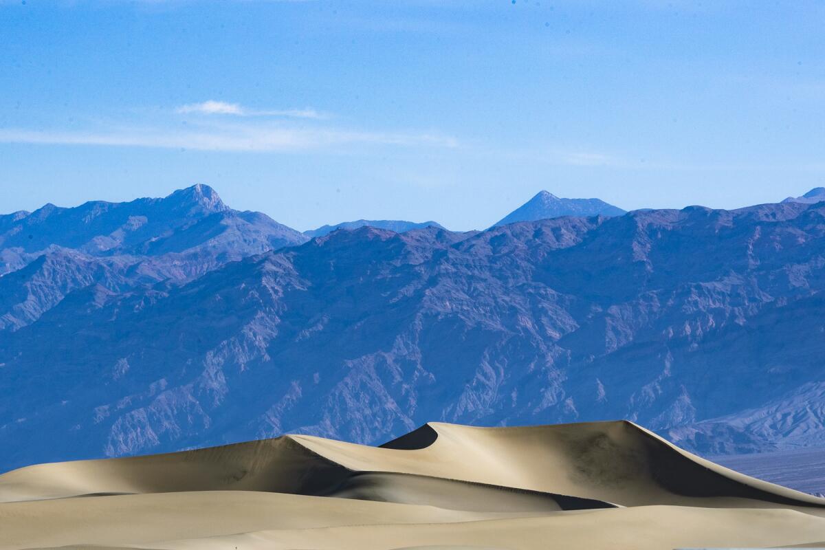 Blue mountains against the sky with sand dunes in foreground