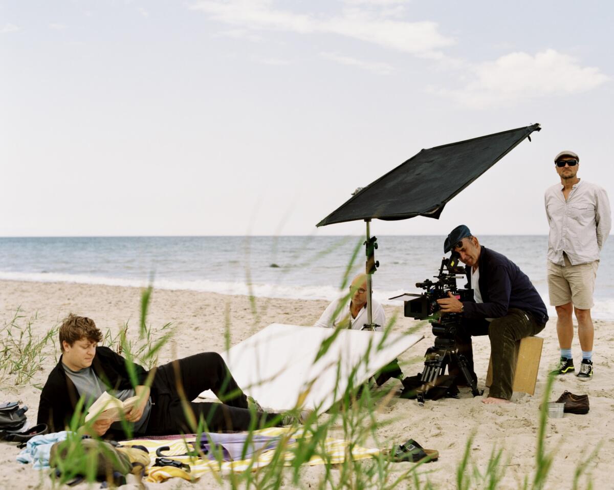 A man films a person on the beach reading