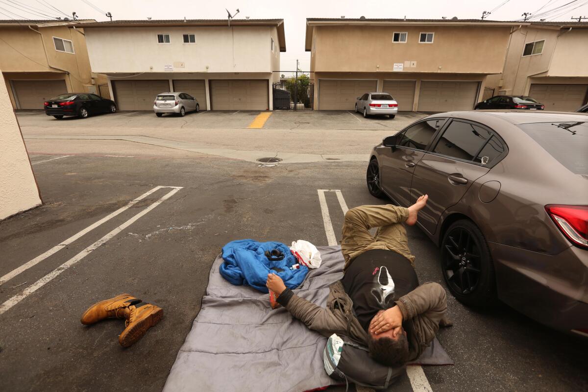 A man rests on a sleeping bag in a parking space in an alley in Torrance.