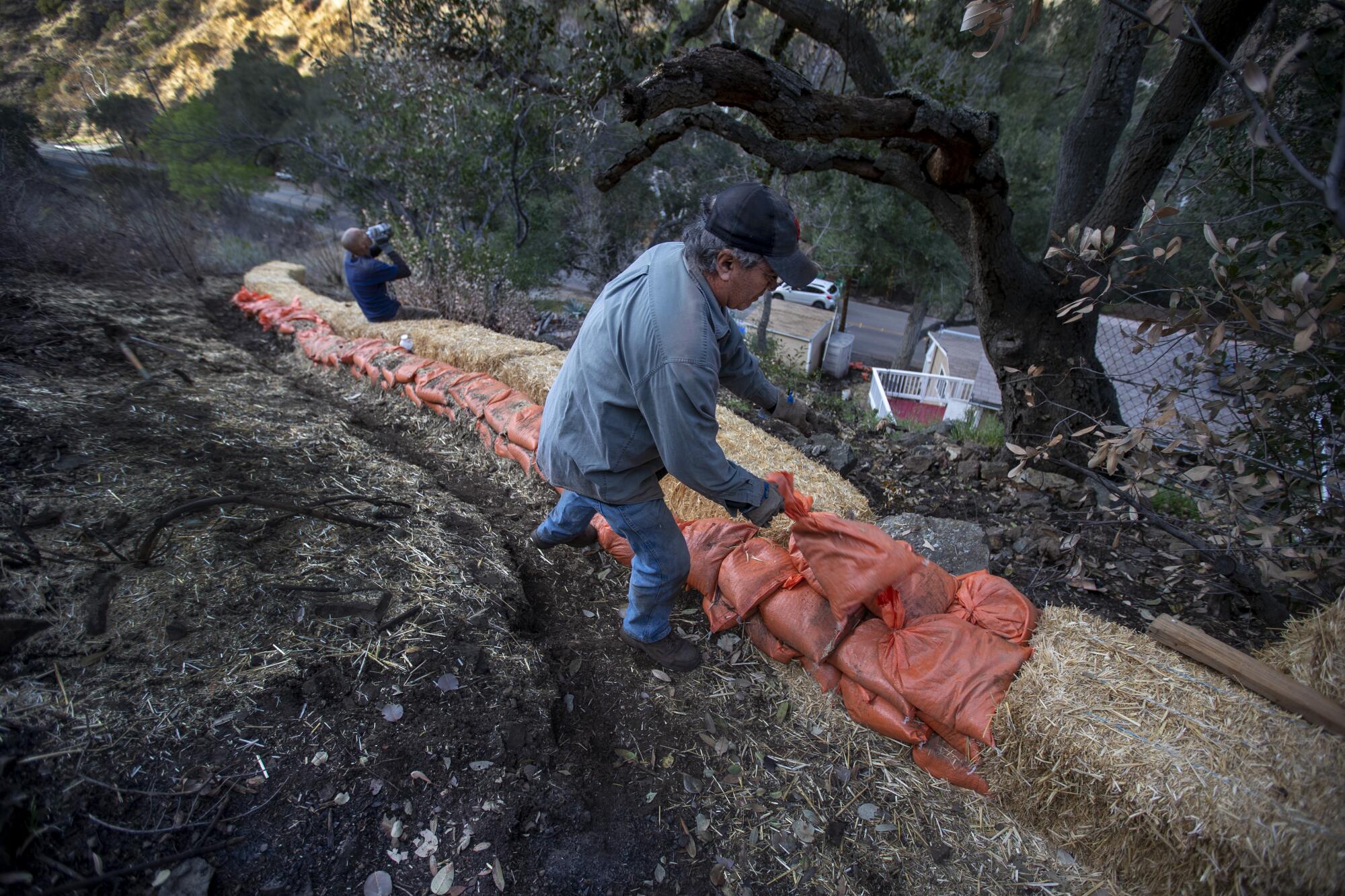 Resident Ambrose Jimenez piles up sandbags while digging a ditch to divert mudslide material away from his home.