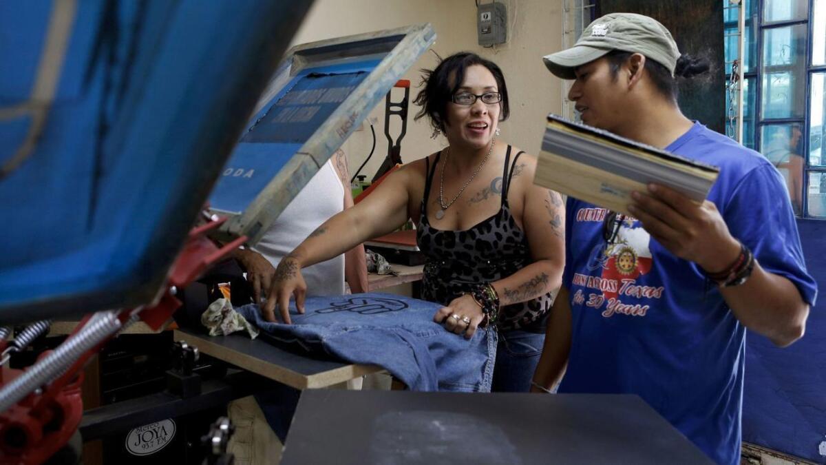 Diego María (der.), habla con Ana Laura López mientras imprime camisetas en una tienda que abrieron junto con otros deportados, en Ciudad de México.