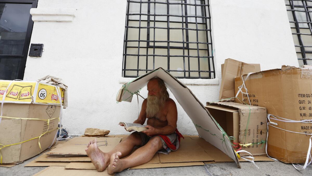 Raymond Byrnes, 71, reads under a cardboard box on Crocker Street in between 3rd and 4th Street on May 17.