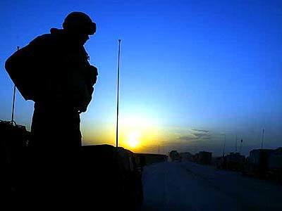 A soldier watches the sunset as convoy of Army vehicles pass through Iraqi desert.