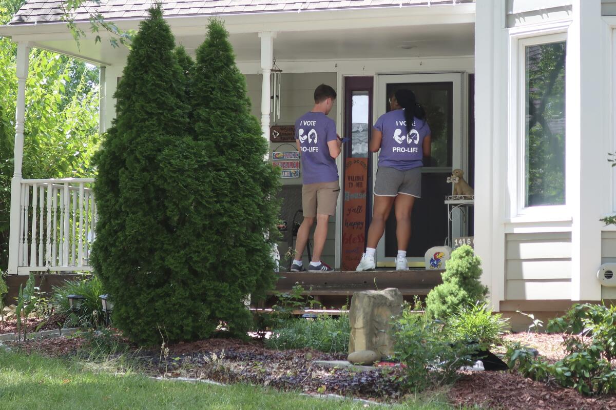 Ben Kennedy, left, and Alyssa Winters, left, wait at a door to speak with prospective voters about a proposed amendment to the Kansas Constitution that would allow legislators to further restrict or ban abortion, Friday, July 8, 2022, in Olathe, Kan. They are among about 300 college students brought into Kansas by the Susan B. Anthony Pro-Life America group, which backs the measure. (AP Photo/John Hanna)