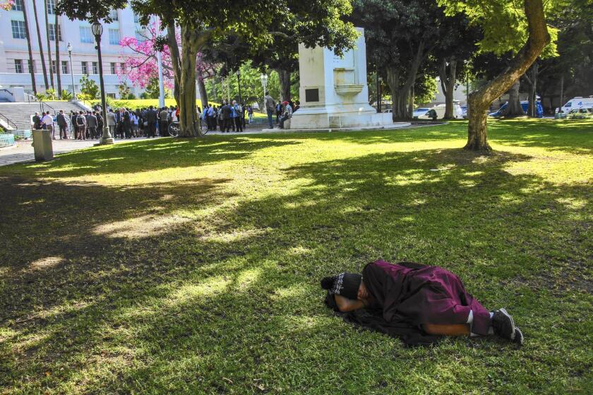 A homeless person sleeps on grass at City Hall as elected leaders announce a plan to declare homelessness in L.A. an emergency and commit $100 million toward the problem.