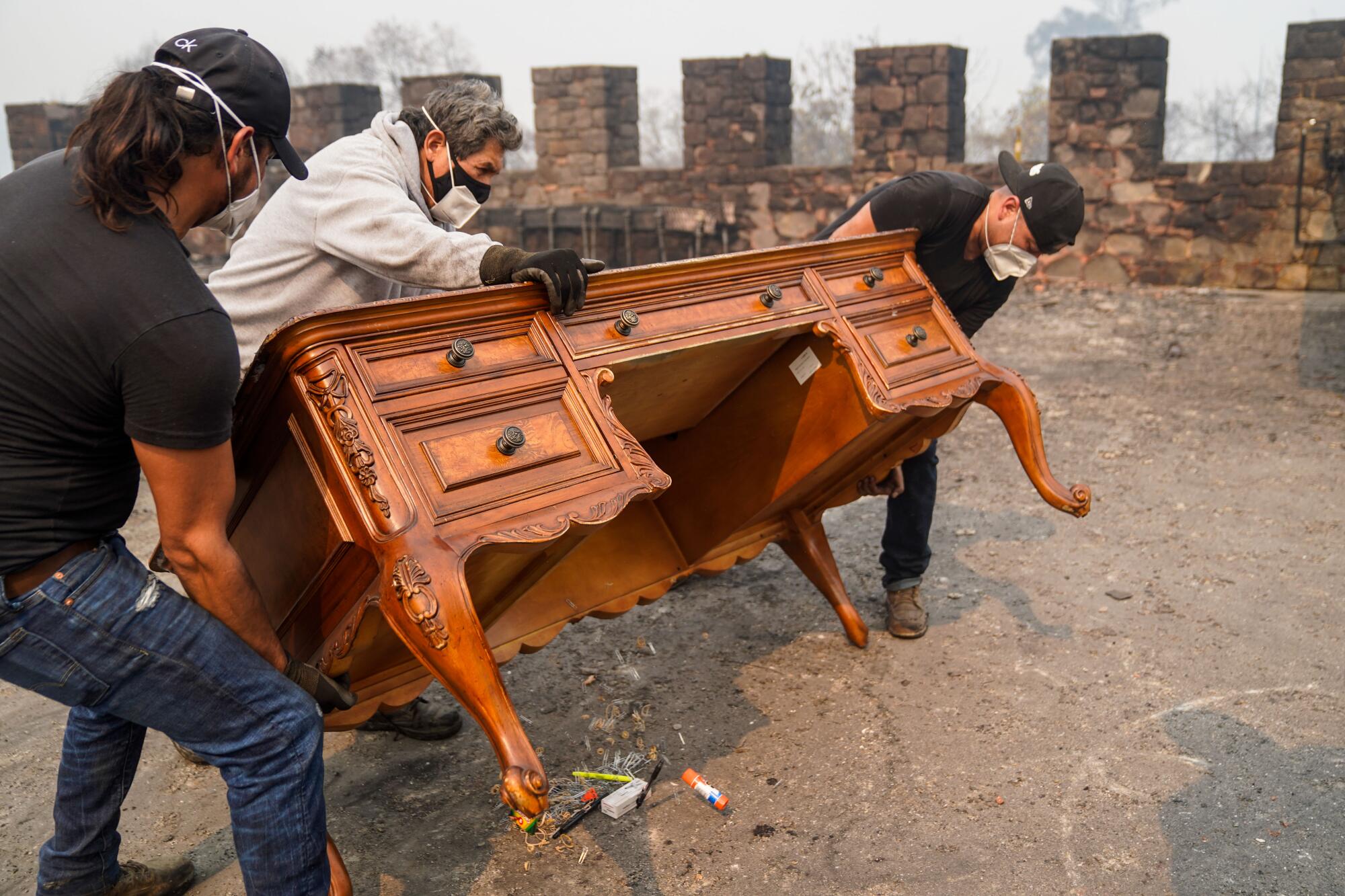 Workers in masks carry a desk recovered from a burned building at a Napa County vineyard.