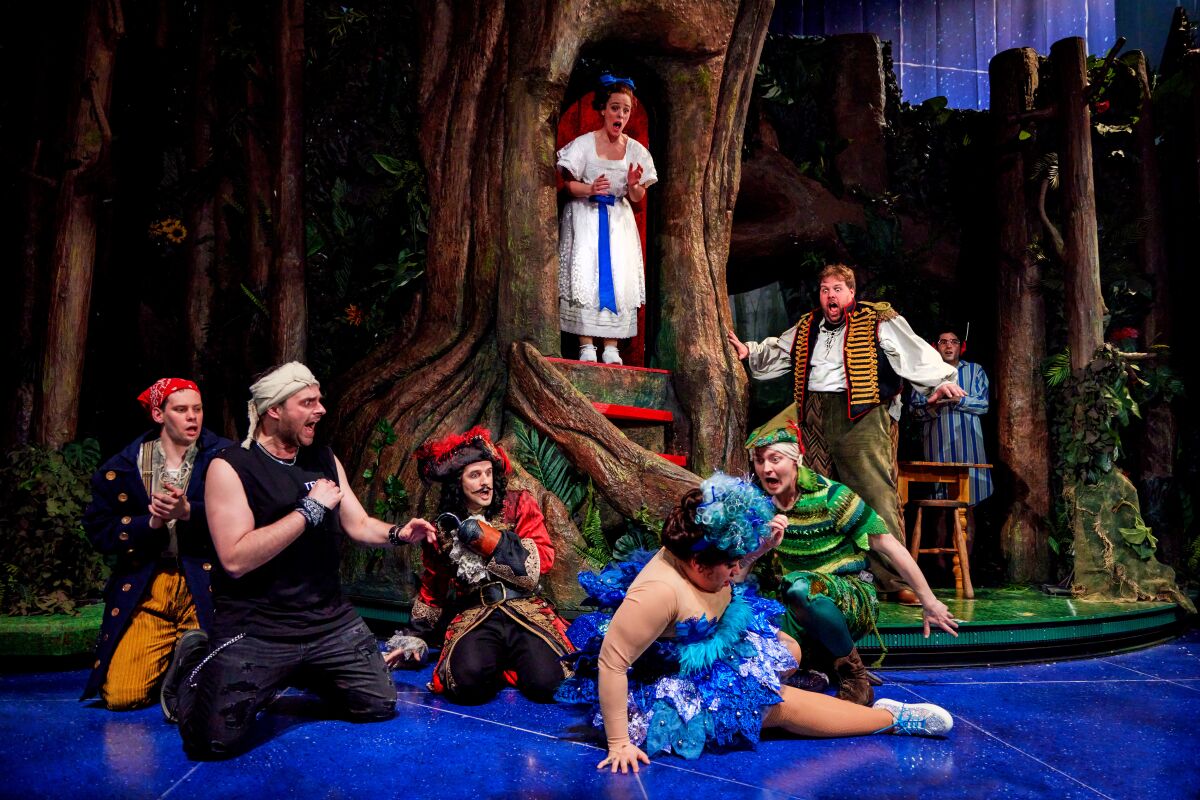 A group of actors in costume — a little girl, a pirate, a fairy and Peter Pan — engage in pratfalls on a theater set.