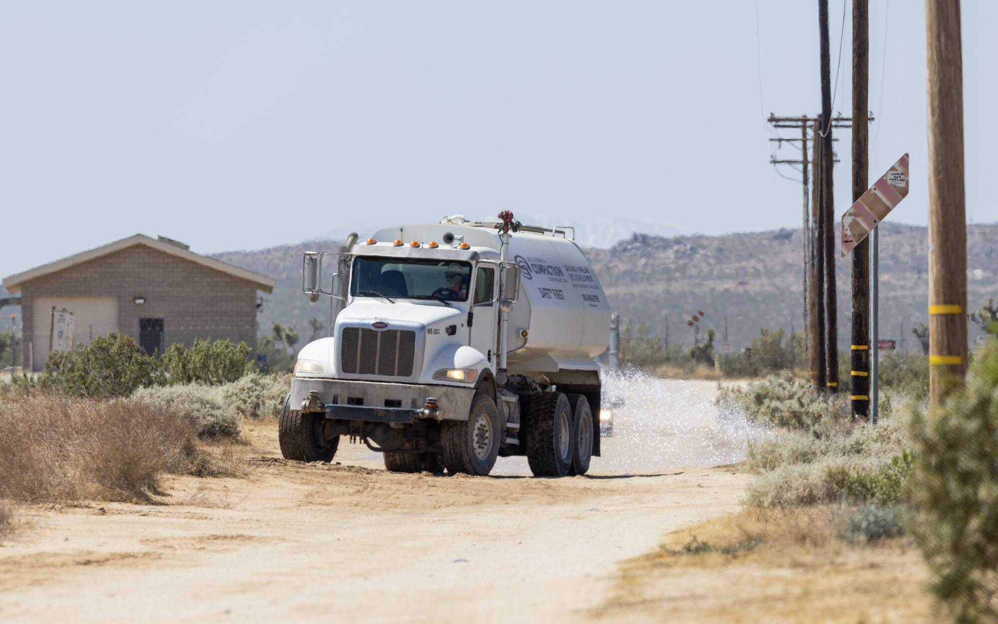 A tanker truck spreads water on a dirt road in the desert.