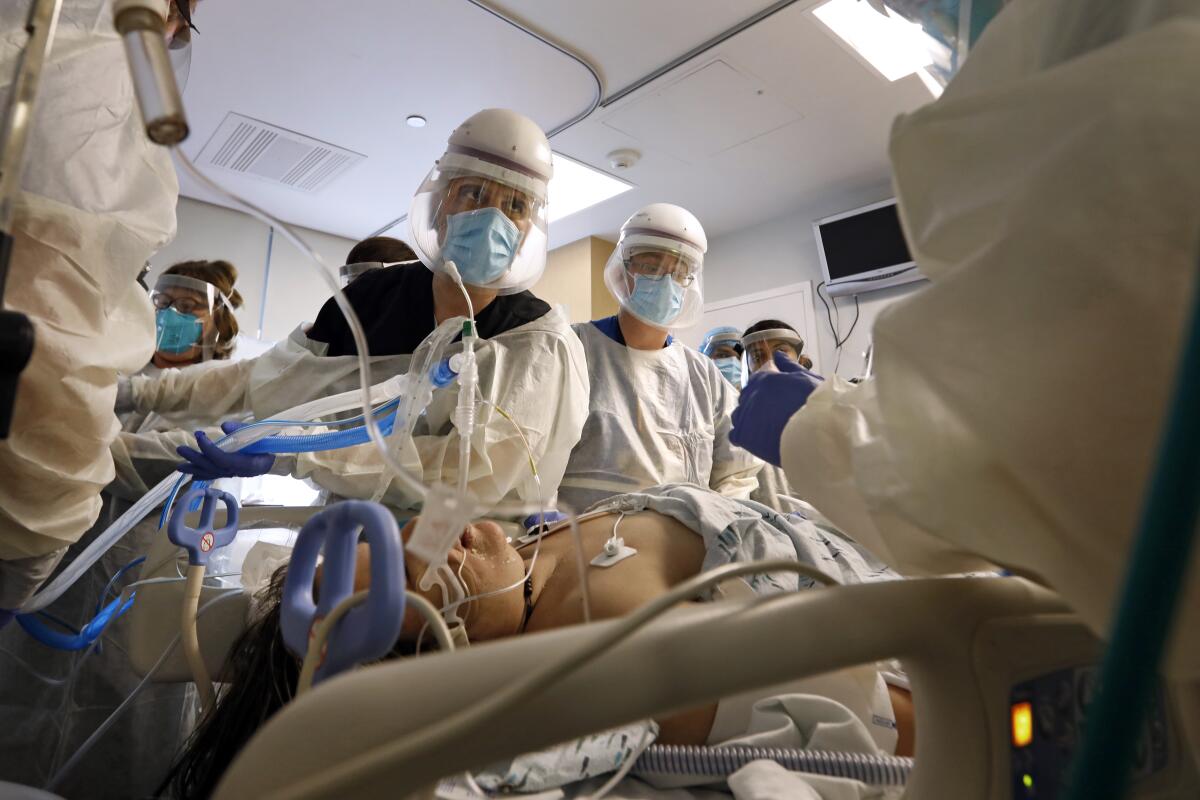 Healthcare workers in face masks, gowns and masks stand over a patient on a hospital bed amid tubes and cords.