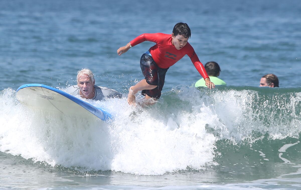 Instructor Tom Swanecamp rides alongside as Christopher Godoy jumps off his board during the Miracles for Kids surf camp Friday at the Newport Pier in Newport Beach.