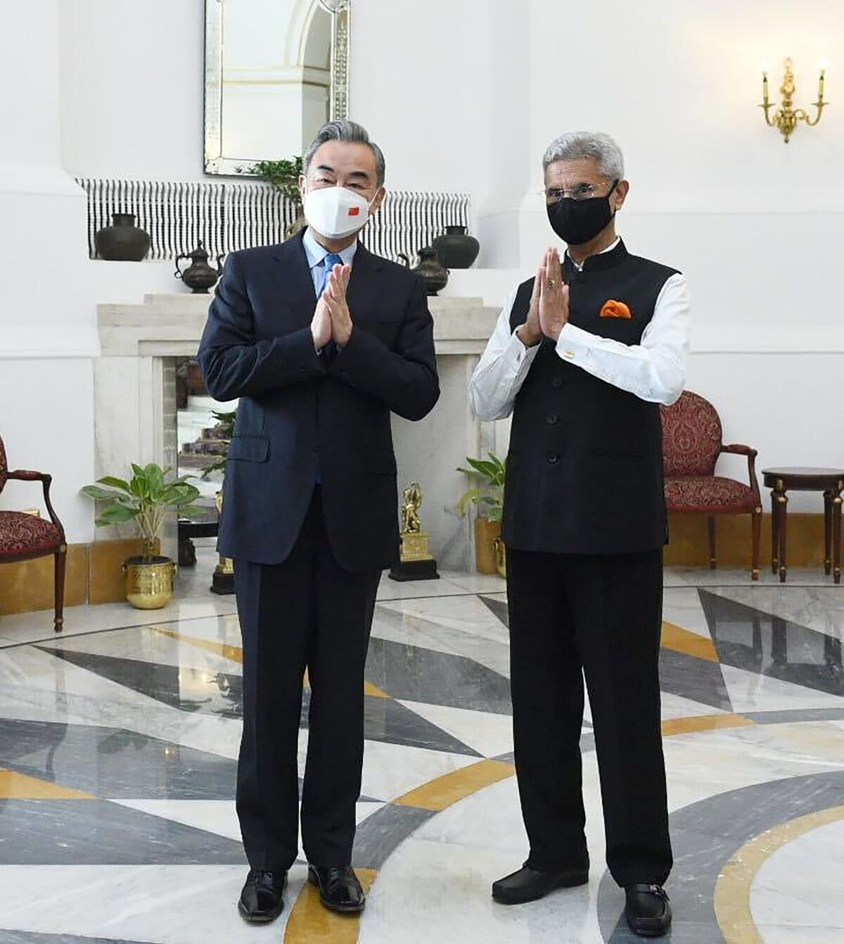 Two men wearing masks pose for a photo with their hands together