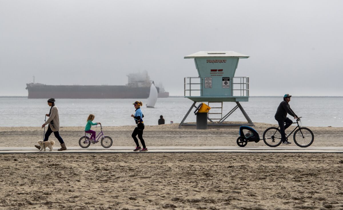 People walk, jog and ride bikes on a beach path in front of a lifeguard tower on an overcast day.