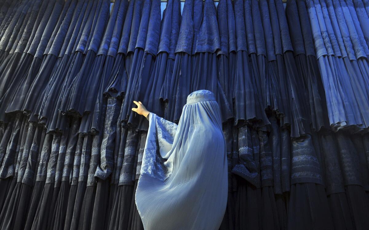 FILE - A woman clad in a burqa looks at other pieces of Afghanistan's traditional, all-encompassing dress at a store in Mazar-i Sharif, north of Kabul, Afghanistan, on Sept. 10, 2015. The Taliban announced they have arrested and will soon sentence an Afghan woman who appeared in a video on social media on Aug. 30, 2022, and said a senior Taliban official forced her into marriage and raped her repeatedly. (AP Photo/Mustafa Najafizada, File)