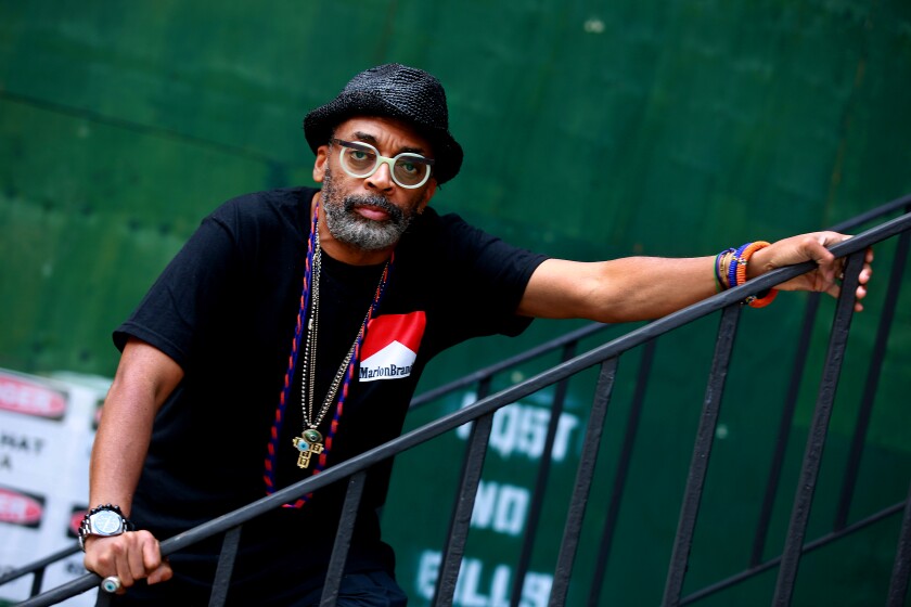 Spike Lee leaning on a staircase railing against a dark green backdrop