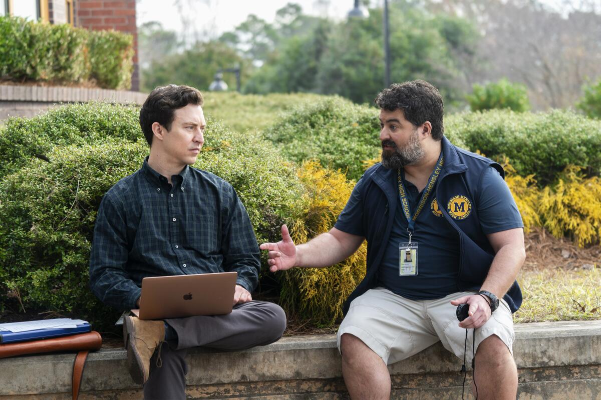 Two men sitting on a retaining wall.