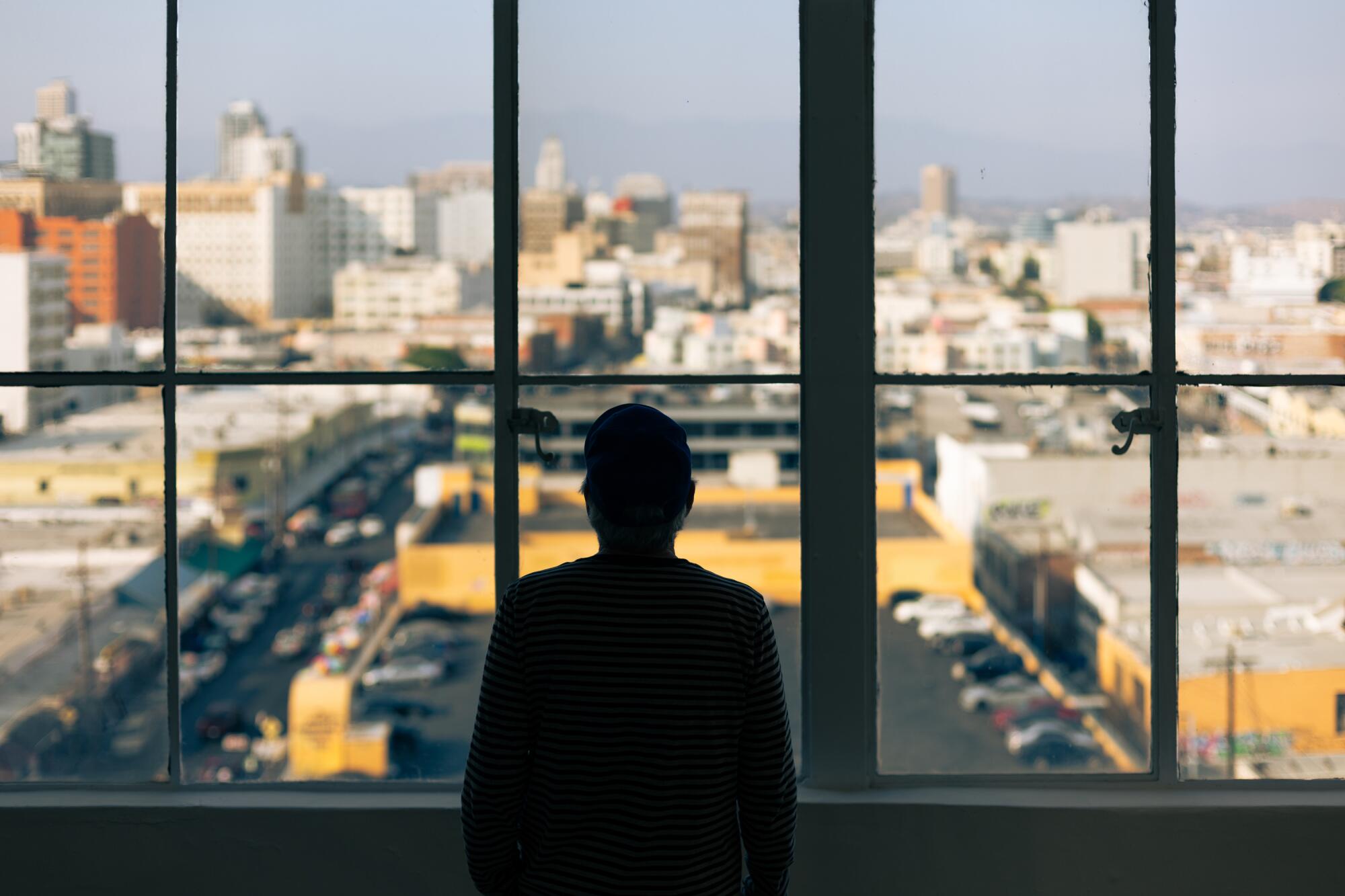 Robbie Conal, seen in silhouette, stands at a window overlooking downtown Los Angeles