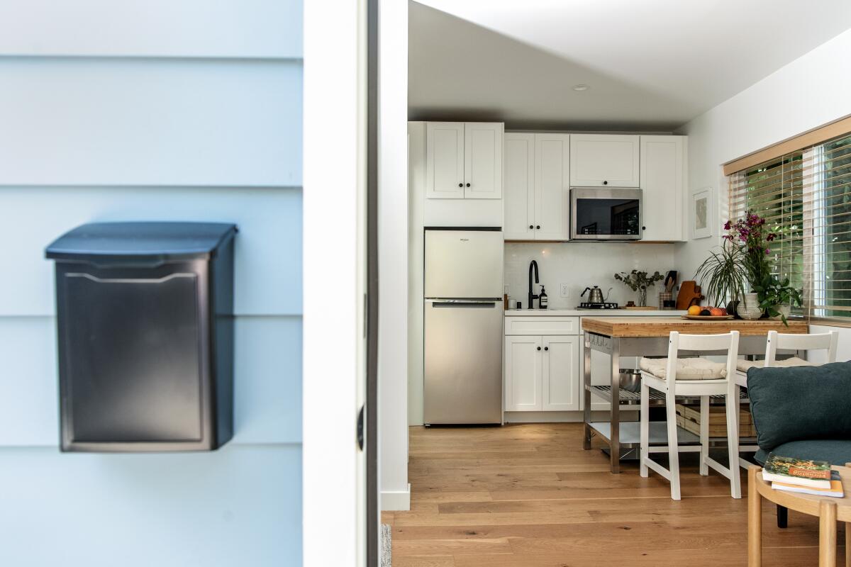 Looking into the kitchen from outside the front door, one sees white barstools at a wood countertop and white cabinets. 