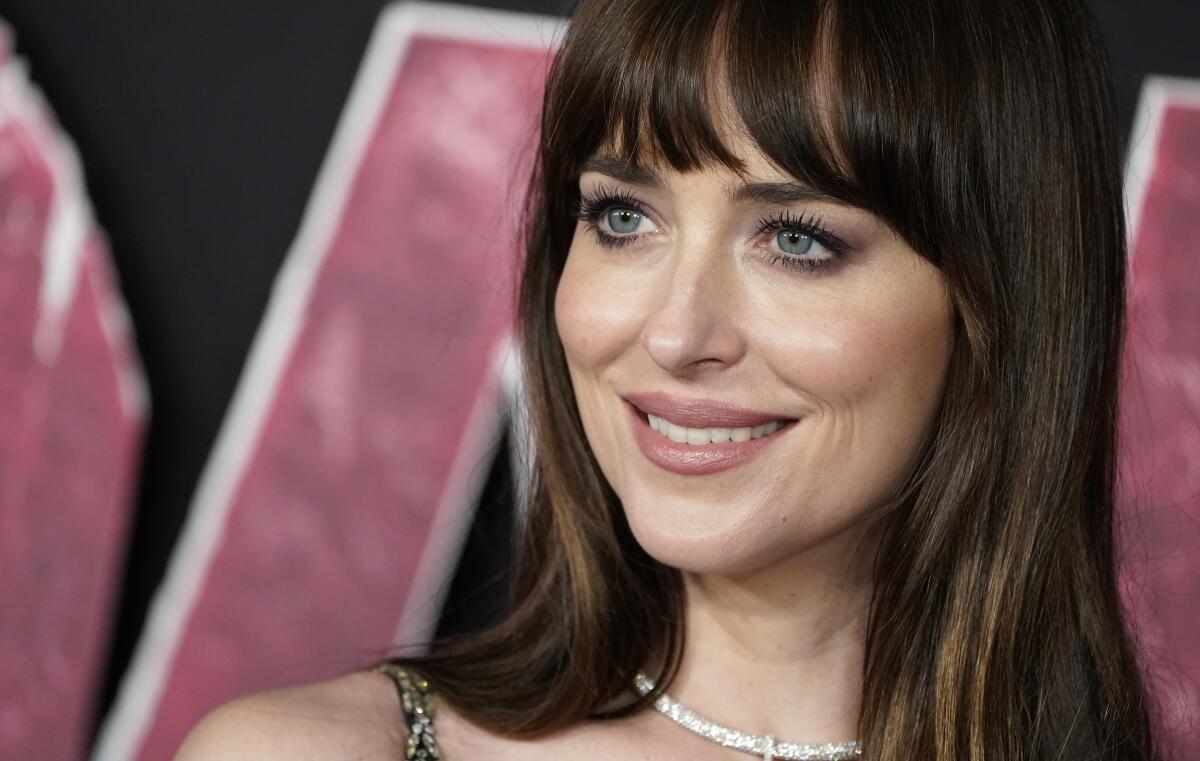 An up-close photo of Dakota Johnson, smiling while standing in front of a backdrop