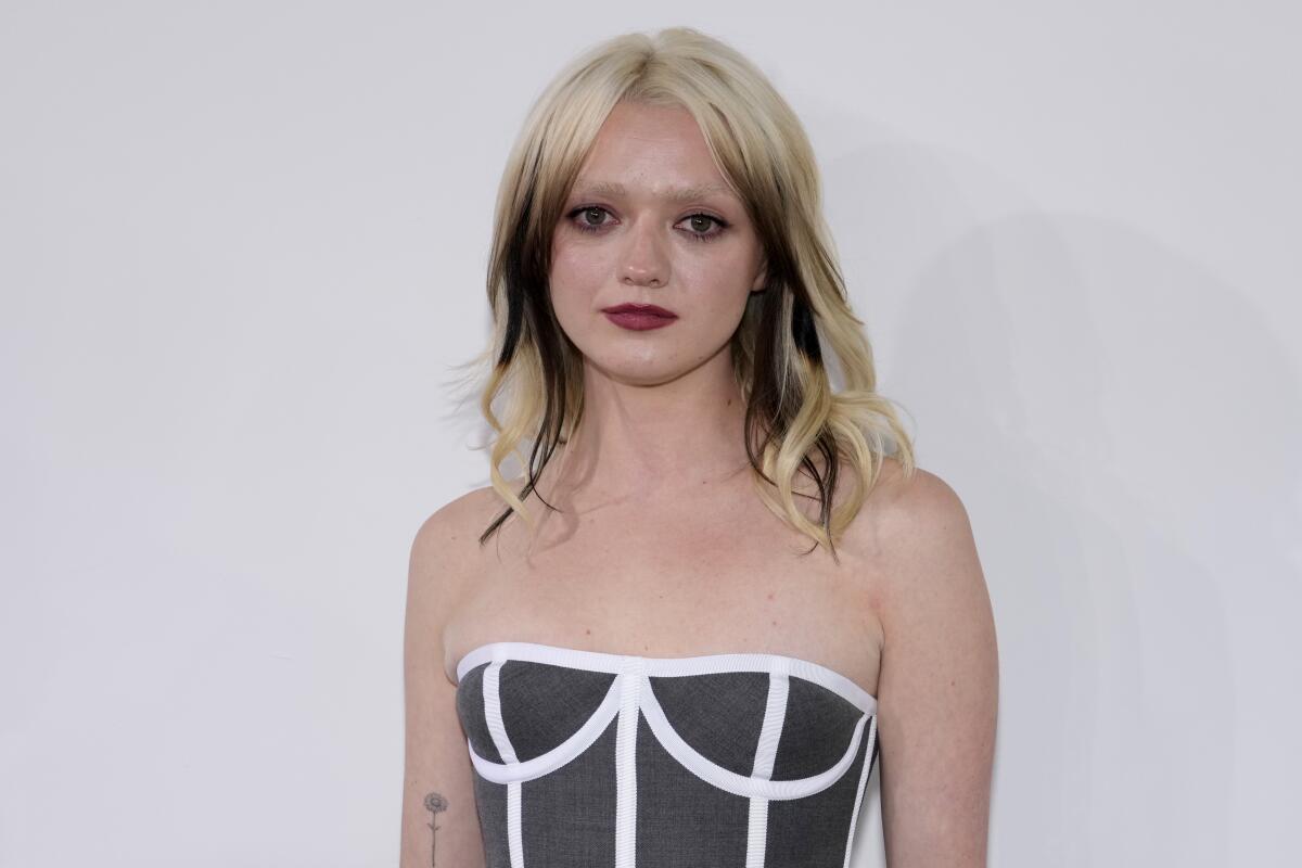 A blond woman wearing a strapless, gray and white top poses