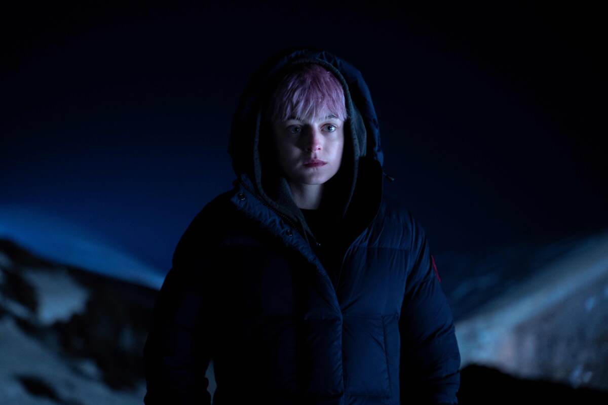 A young woman with pink hair in a heavy-duty winter coat on an Icelandic night.