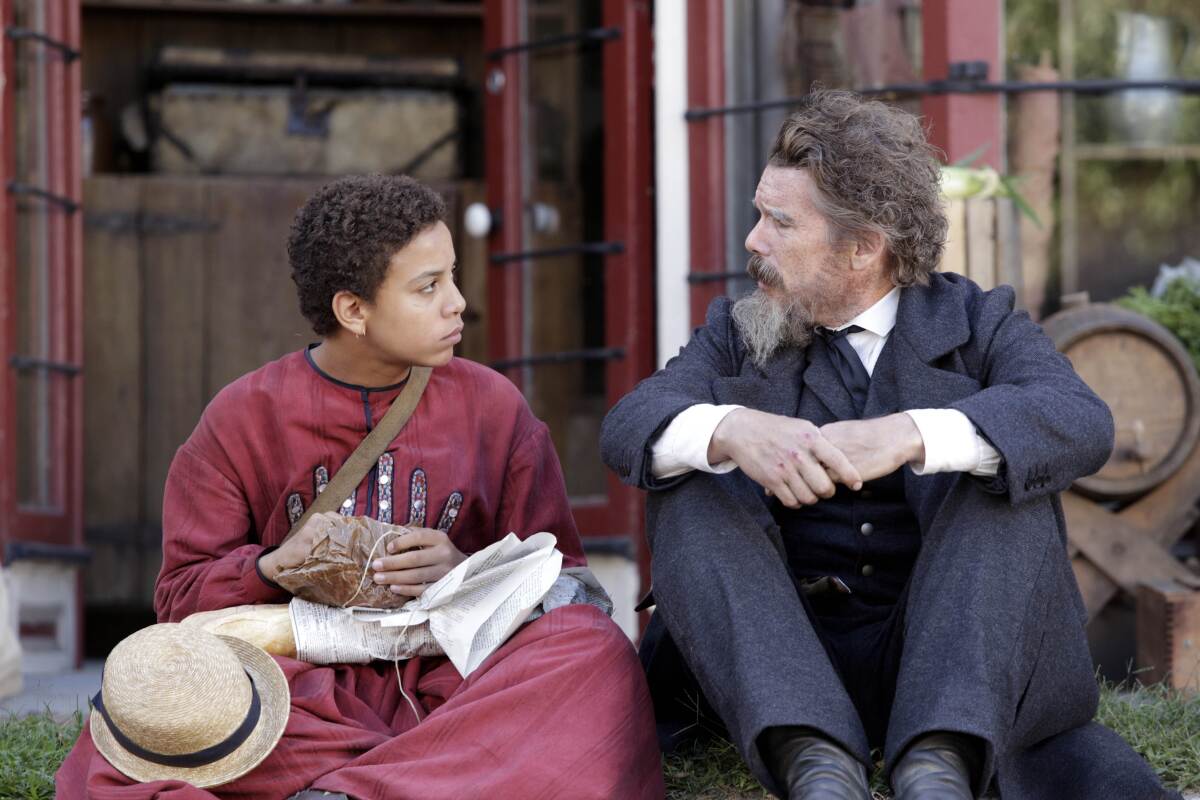 Joshua Caleb Johnson sits on a lawn beside Ethan Hawke in a scene from "The Good Lord Bird."