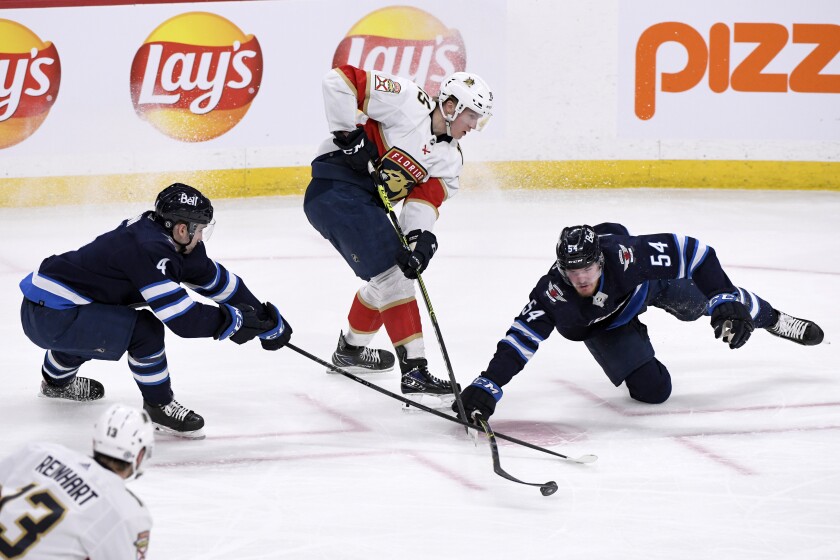 Florida Panthers' Anton Lundell (15) passes the puck between Winnipeg Jets' Neal Poink (4) and Dylan Samberg (54) during the first period of an NHL hockey game in Winnipeg, Manitoba, Tuesday, Jan. 25, 2022. (Fred Greenslade/The Canadian Press via AP)