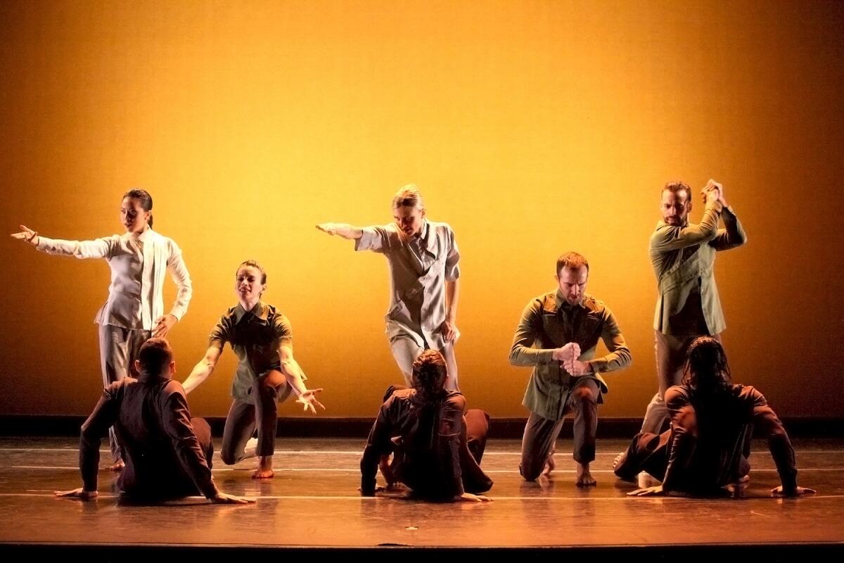 Men and women dancers onstage, some sitting on the floor, some standing facing them and gesturing.