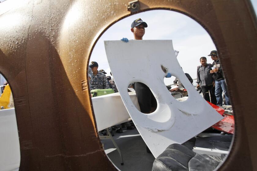 An Indonesian navy ship crew member holds a piece of a window panel recovered from the wreckage of AirAsia Flight 8501, during a news conference in Surabaya, Indonesia, on Monday.