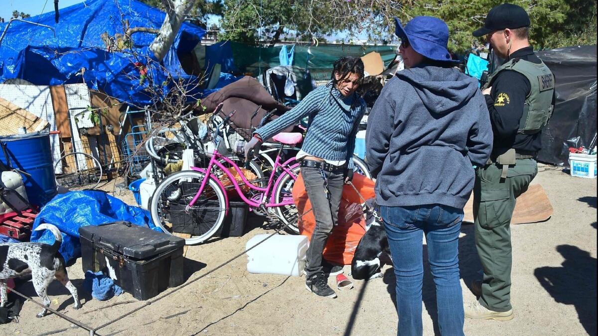 An Orange County Sheriff's deputy and a social worker speak with a woman at the homeless encampment beside the Santa Ana River in Anaheim in February.
