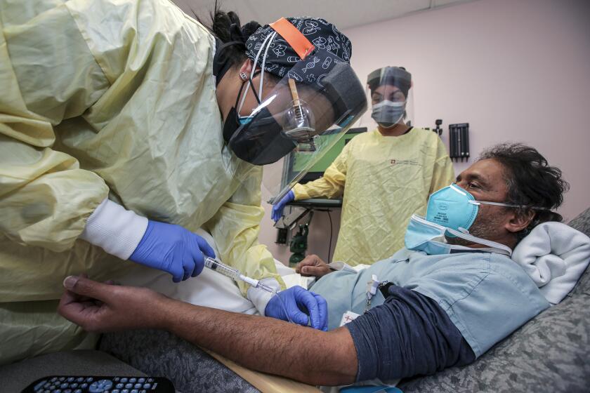 Victorville, CA - December 17: Nurse Salina Padilla, left, prepares Dr. Prabakar Tummala for Bamlanivimab, monoclonal antibody infusion at Desert Valley Hospital on Thursday, Dec. 17, 2020 in Victorville, CA. (Irfan Khan / Los Angeles Times)