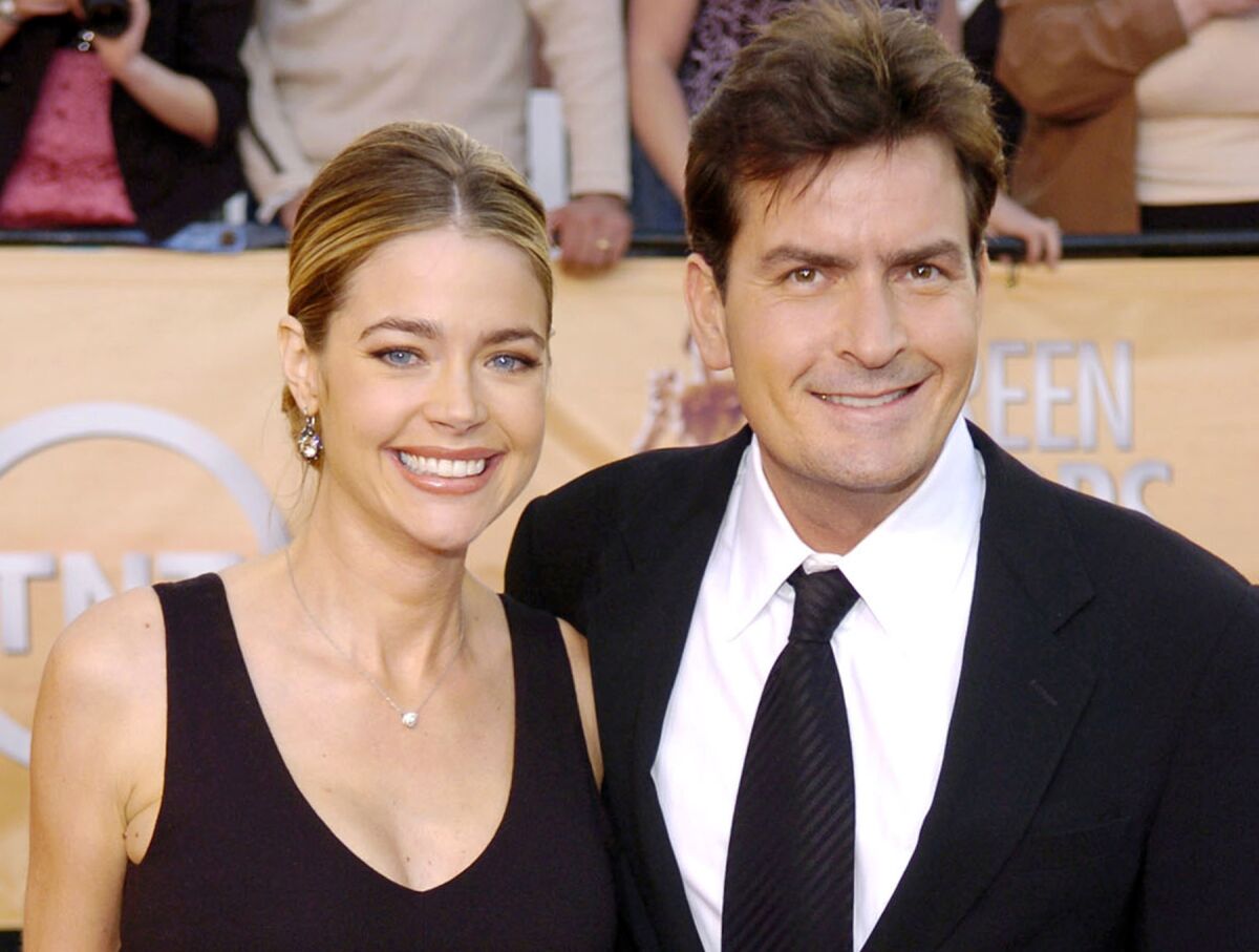 Denise Richards and Charlie Sheen smile while posing together in black formal attire.