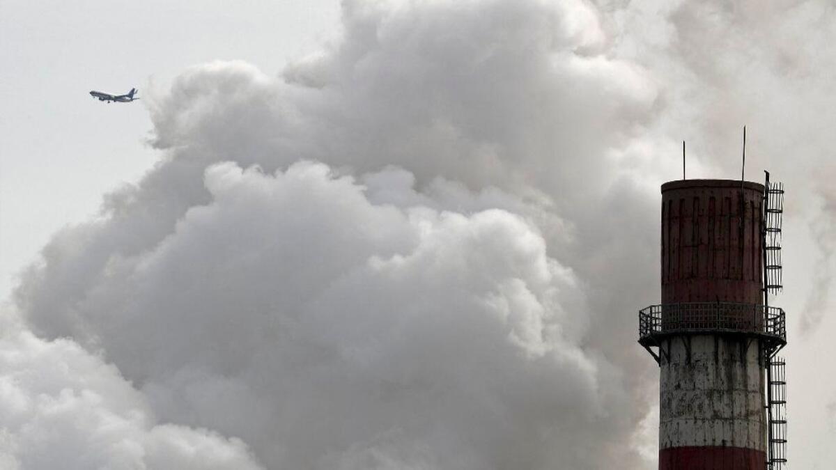 A passenger airplane flies behind steam and white smoke emitted from a coal-fired power plant in Beijing.