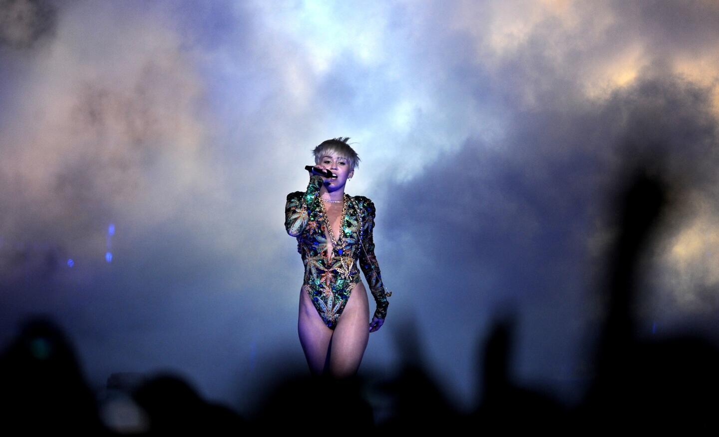 Miley Cyrus emerges from a cloud of smoke wearing a shiny green one-piece reminiscent of the 1990s.
