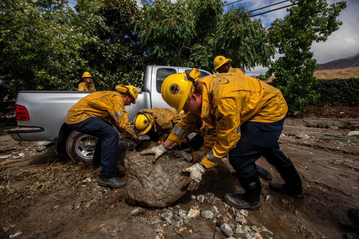 People in yellow jackets and helmets push boulders next to a pickup truck.