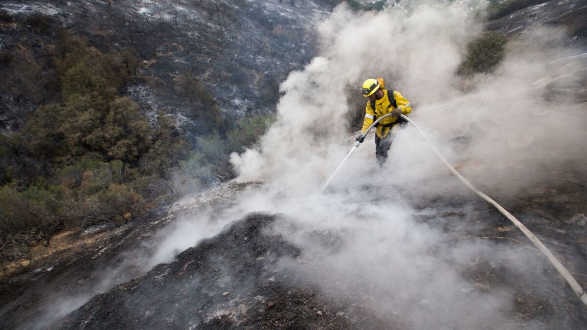L.A. County firefighter Kevin Sleight extinguishes hot spots while battling the La Tuna fire along Crestline Drive in Los Angeles on Sunday.