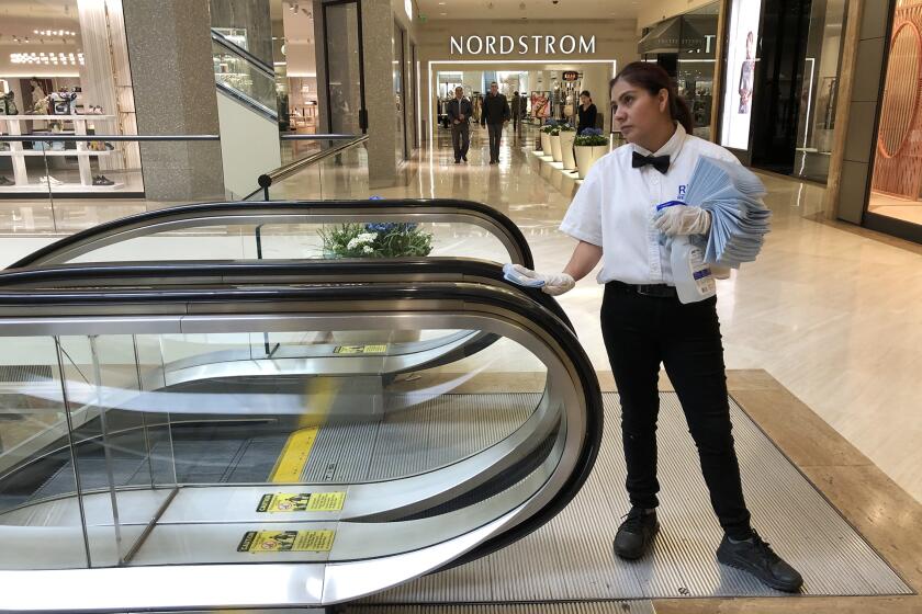 An employee at South Coast Plaza in Costa Mesa disinfects the hand rails of an escalator on Monday, March 16.
