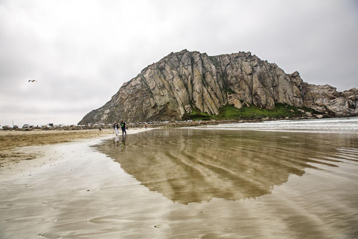 Morro Rock reflected on the wet sand in March. Reports of 18- to 20-foot swells along Morro Bay on Monday forced officials to ban mariners from entering the harbor.