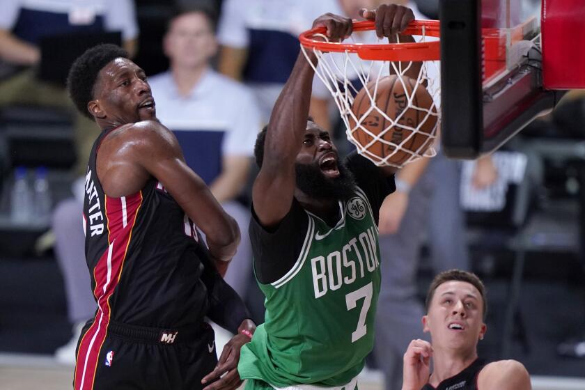 Boston Celtics guard Jaylen Brown (7) dunks the ball between Miami Heat's Bam Adebayo, left, and Duncan Robinson.