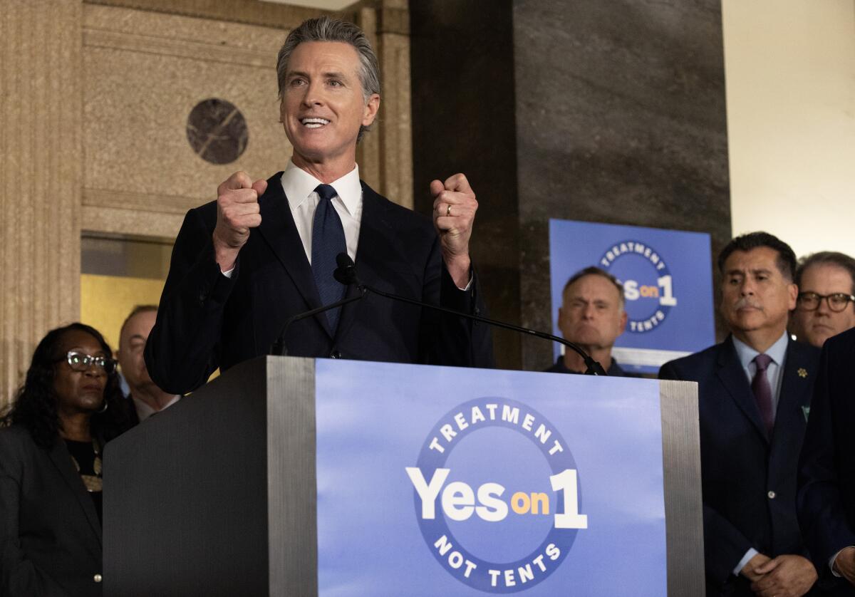 Democratic Gov. Gavin Newsom speaks at a lectern covered with a sing saying Yes on 1 Treatment Not Tents