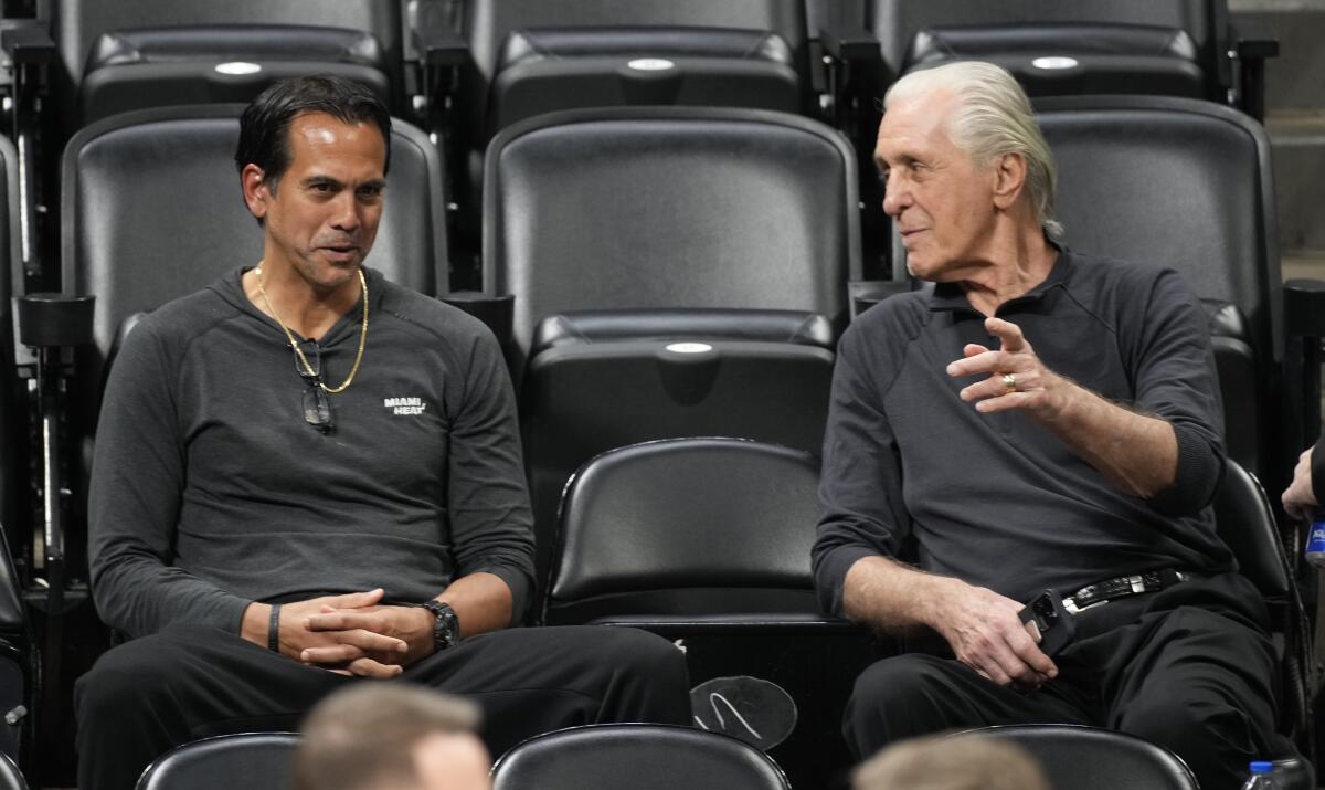 Erik Spoelstra and Pat Riley sit in the stands talking.