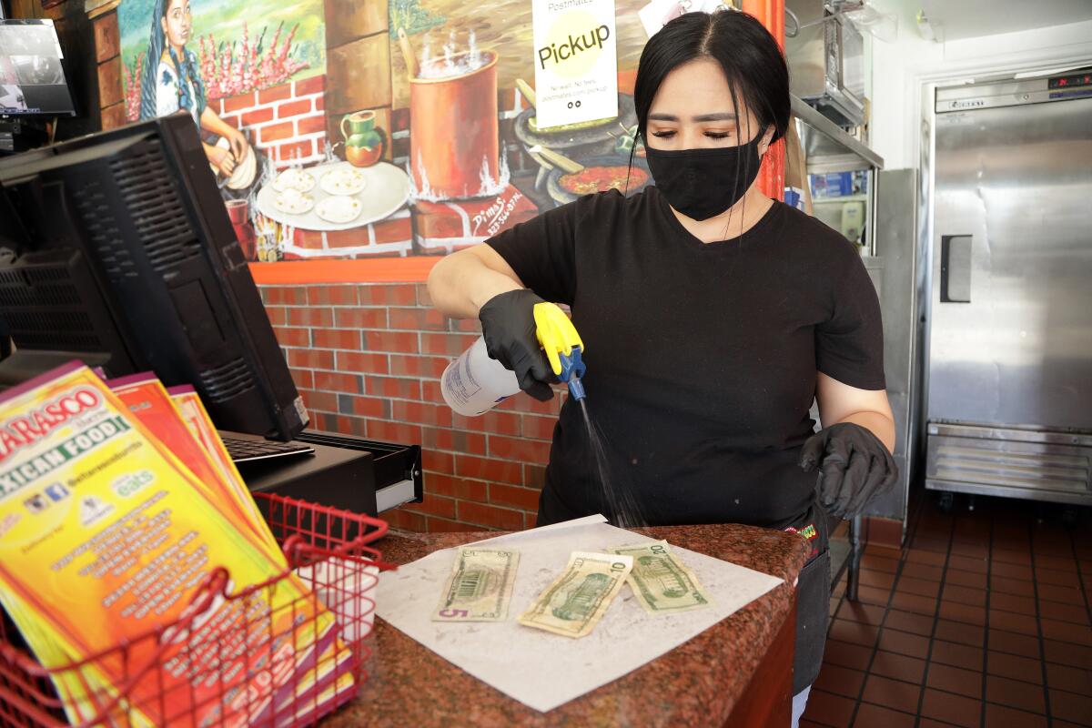 Maricela Moreno, manager at El Tarasco in Venice, disinfects cash at the restaurant on Wednesday,. She said a lot of customers pay with Apple Pay or credit cards. 