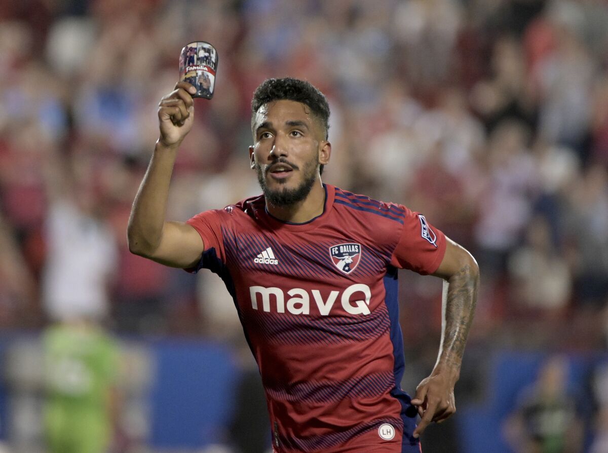 FC Dallas forward Jesus Ferreira (10) celebrates a goal against the Seattle Sounders while holding photos of his family on his shin guard in the second half of an MLS soccer match Saturday, May 7, 2022, in Frisco, Texas. (Matt Strasen/The Dallas Morning News via AP)