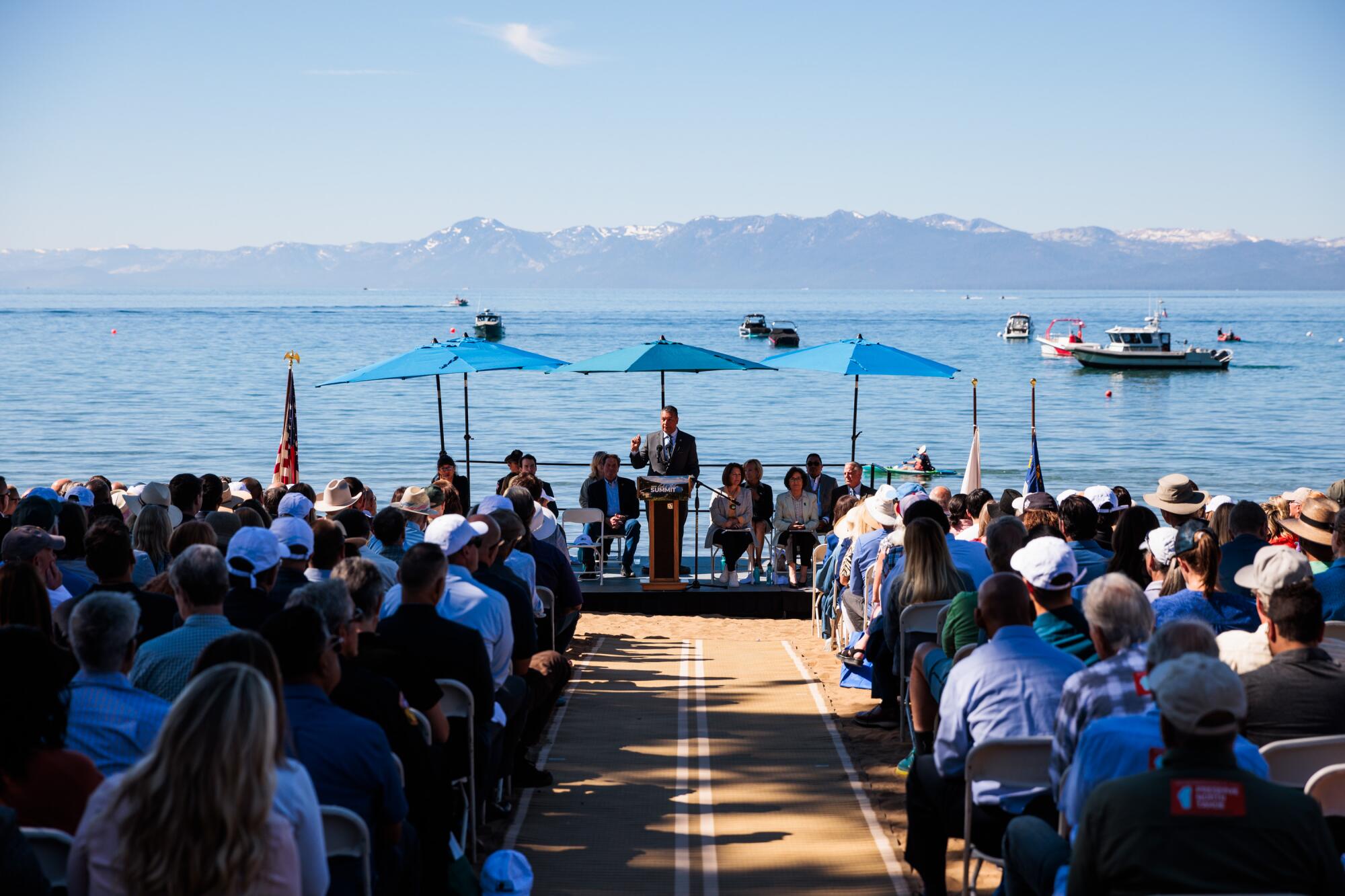 Seated people look at speaker at a lectern by a body of water.