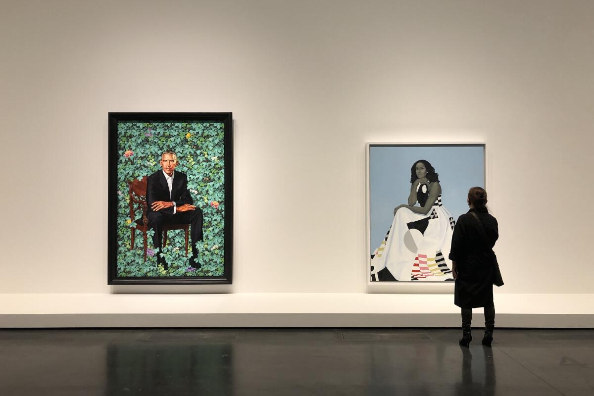 A woman stands before large, colorful paintings of Barack and Michelle Obama