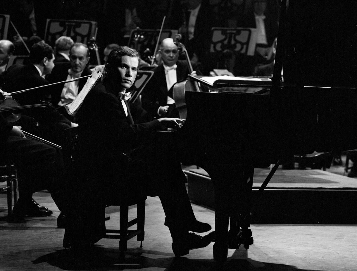 A man sits at a piano as other musicians sit behind him.
